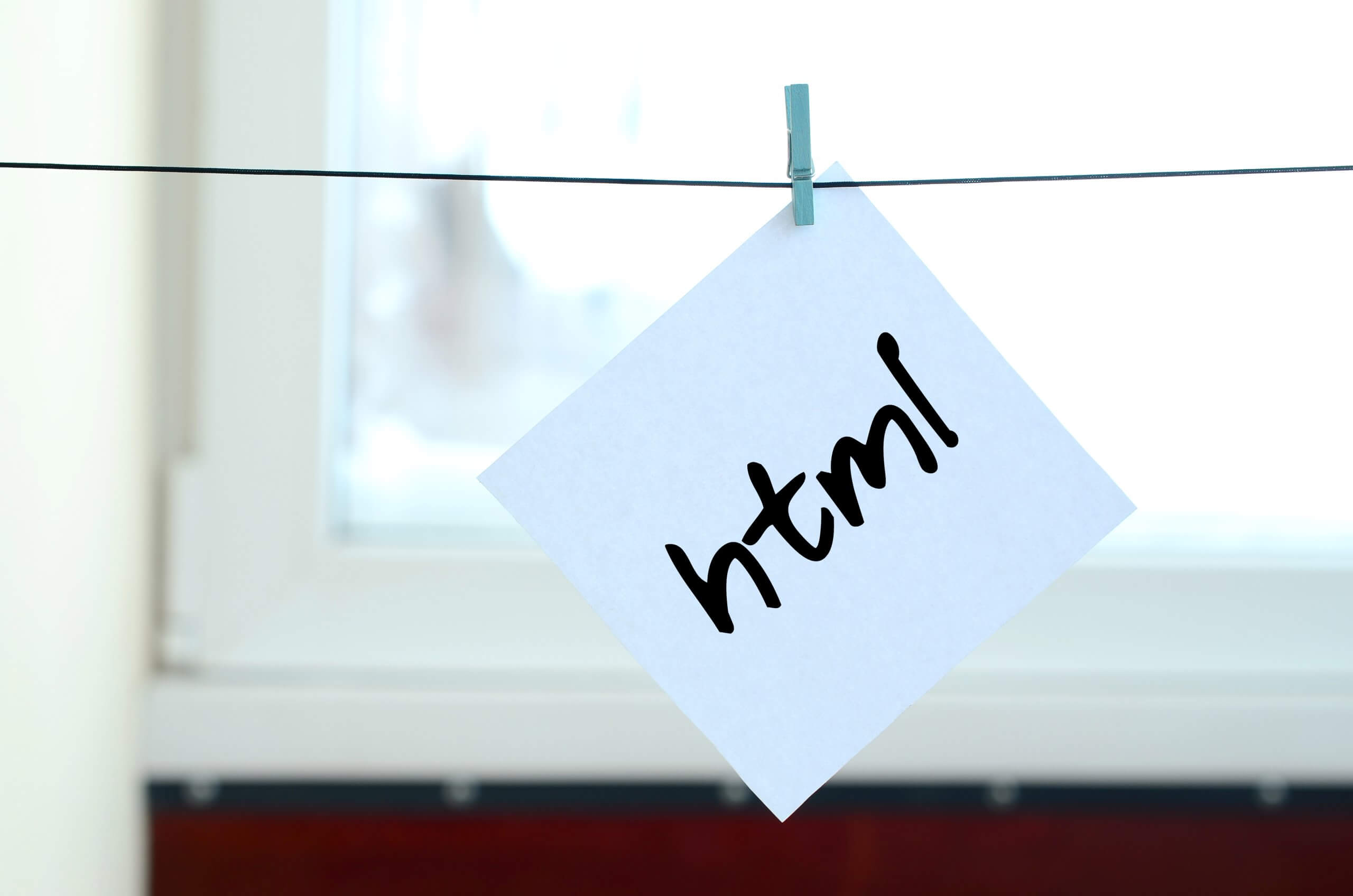 Html. Note is written on a white sticker that hangs with a clothespin on a rope on a background of window glass